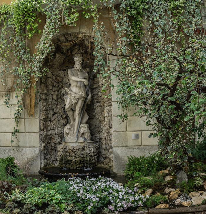 Things to do in Trento Italy: a Neptune statue in an alcove, greenery draped in front