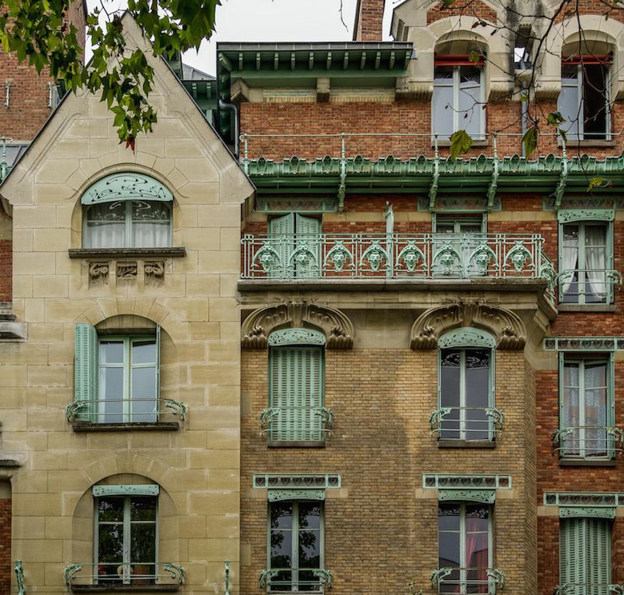 Art Nouveau in Paris: Brick and stone house with aqua green iron designs around the windows, the gutters, the balconies