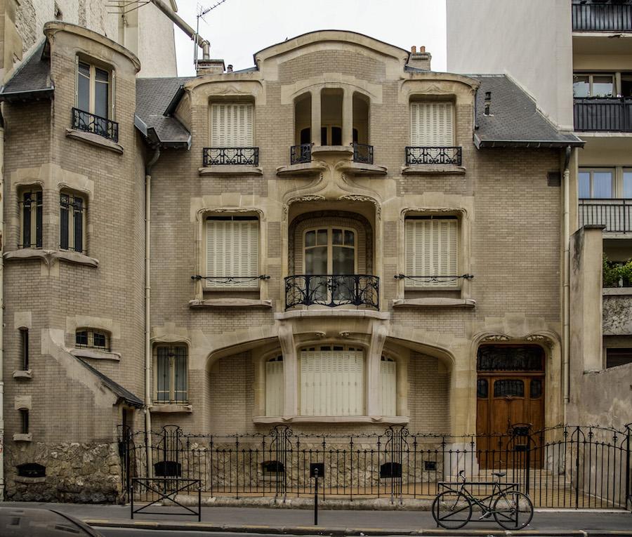 Art Nouveau in Paris - stone and brick house with lacy iron work for window balconies. Beige tones of the house. Architect Guimard
