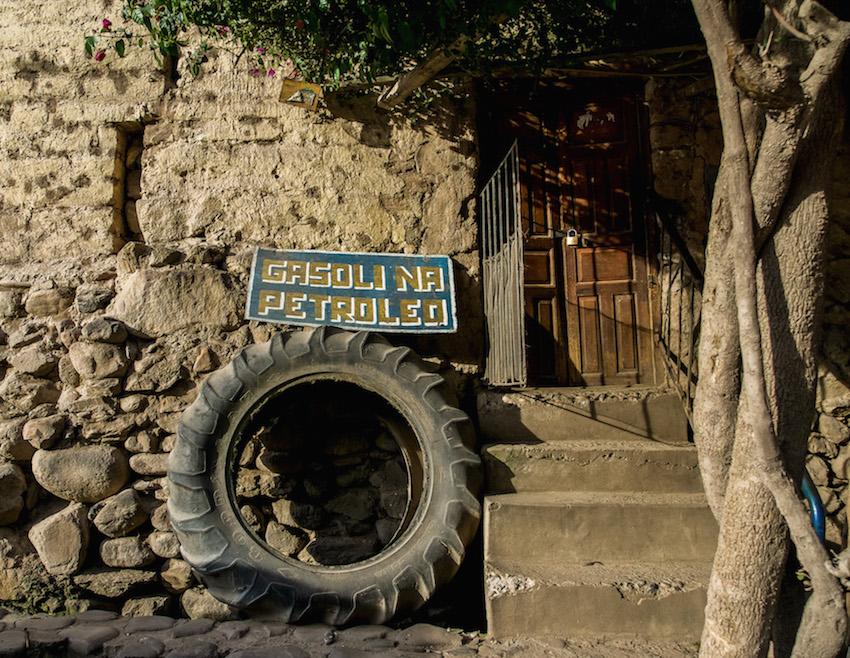 Big old tire leaning against building with sign: GASOLINA PETROLEO