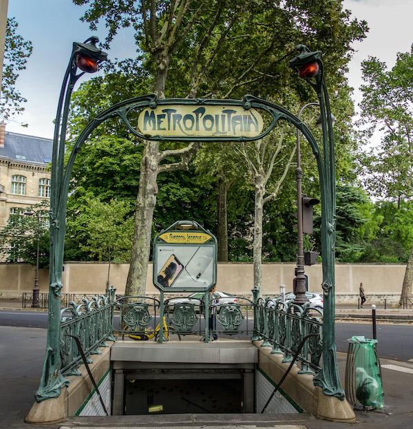 Art Nouveau in Paris - the metro entrance. a tall iron decorative post on either side of the stairs down. The top of the posts have orange lights