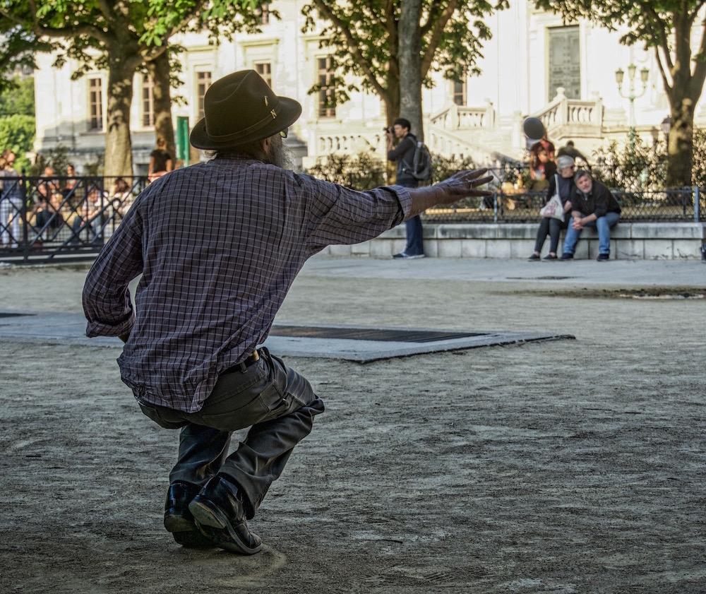 Travelling to Paris alone: Petanque player squatting and tossing the ball