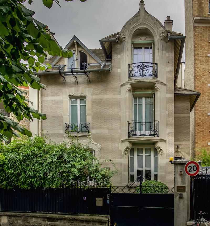 Art Nouveau in Paris 16: Beige toned house, asymmetrical windows which are different shapes and sizes. Balconies stunning wrought iron designs