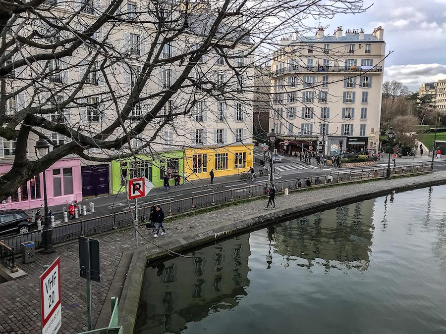 Canal Saint-Martin Paris: pink. lime green and yellow store fronts behind the bare trees