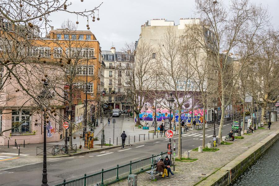 Canal Saint-Martin Paris: bare trees reveal street art. 2 men on a park bench