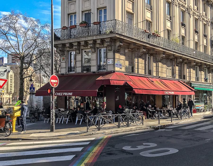Chez Prune in Paris 10; red awnings on the cafe and rainbow stripes on the road.