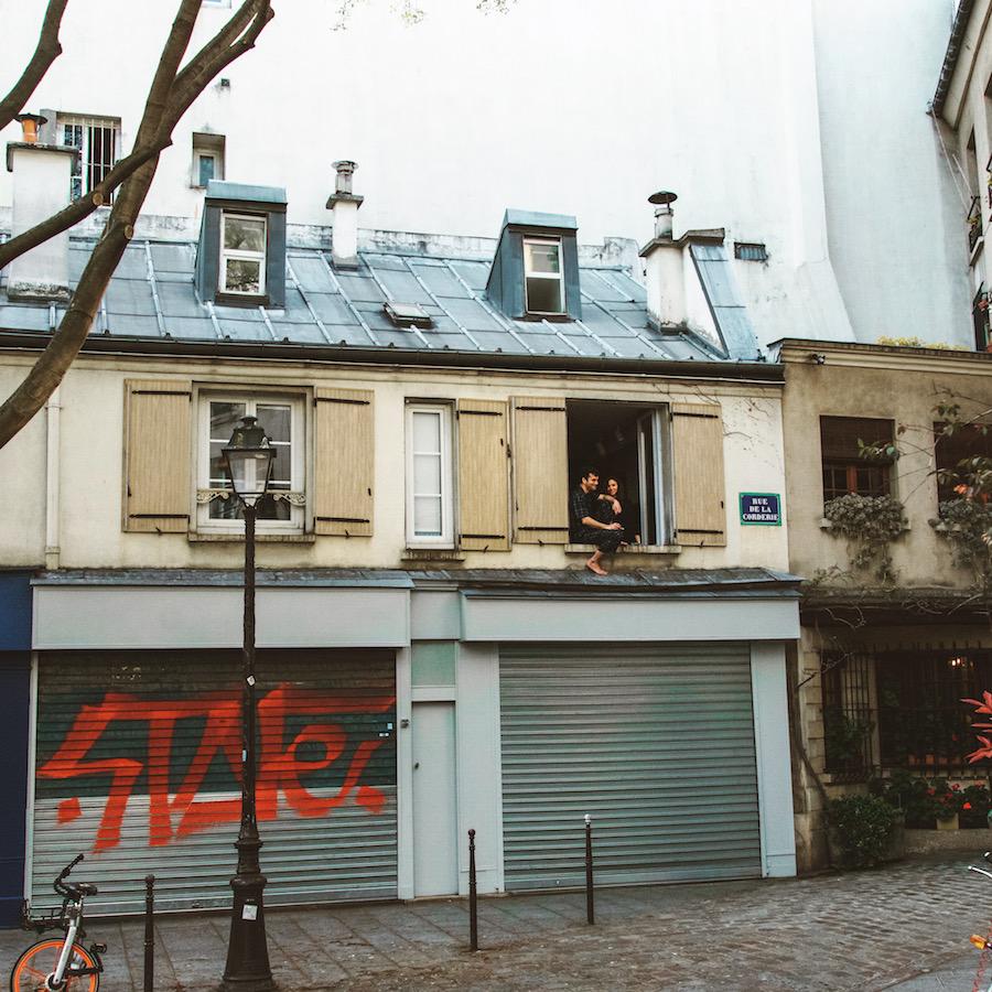 Paris during Coronavirus: a couple sits half out their second storey shuttered window 