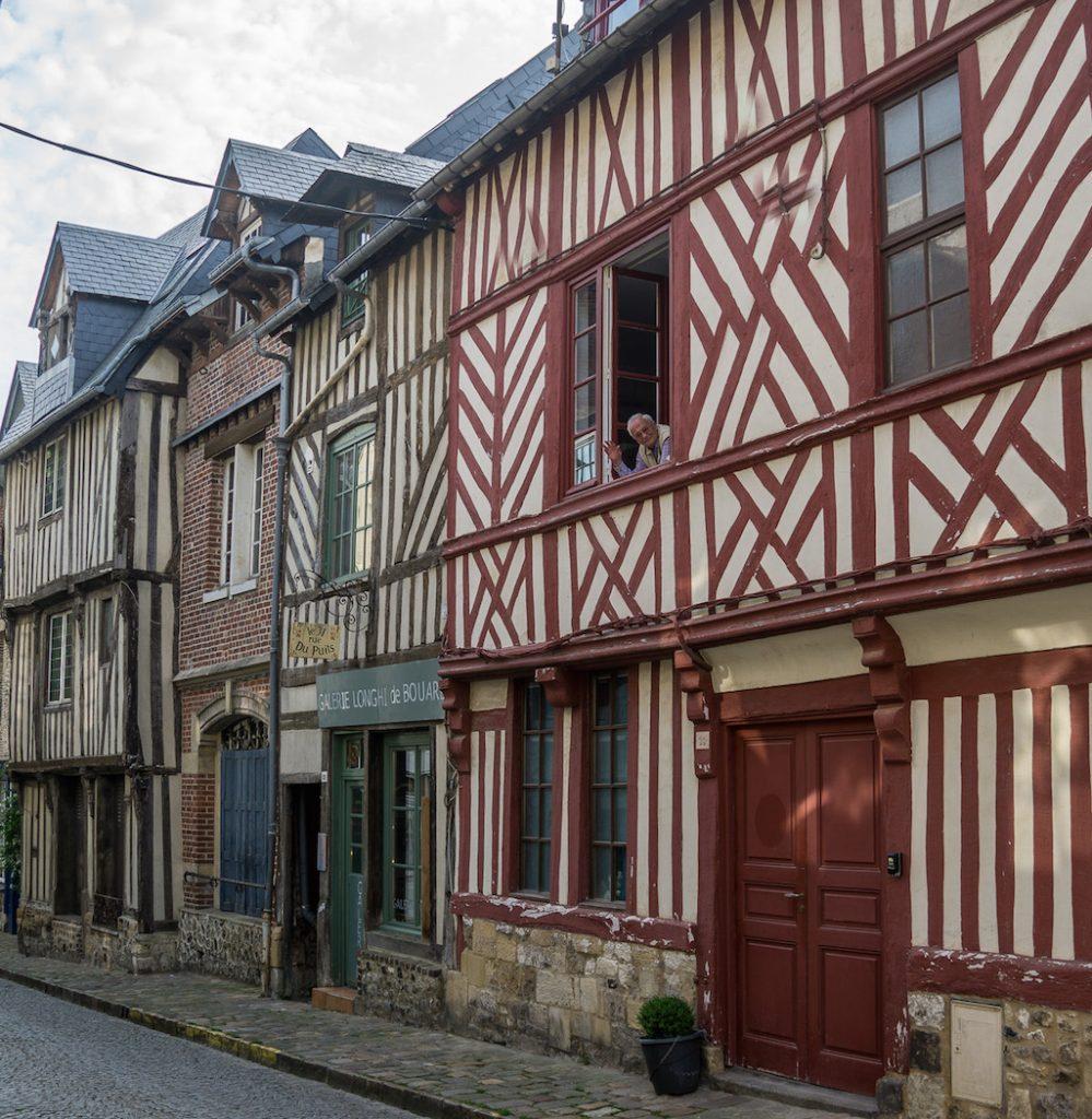 Honfleur France - half timbered houses in red and green. Man waving out the upper window