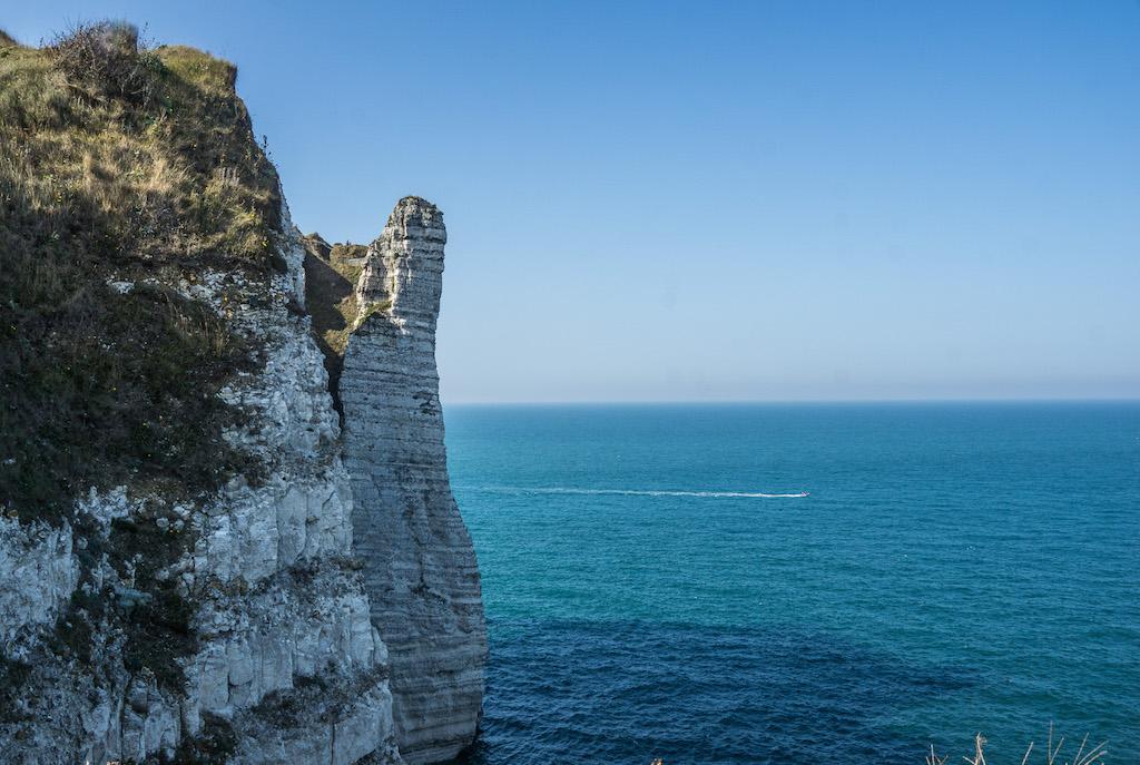 cliffs of Etretat and the blue waters of the sea. A boat zipping by in the distance. 
